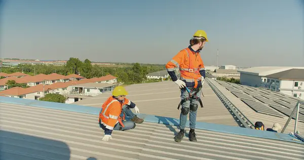 Solar engineers team in safety harnesses are installing panels on the roof of a factory building