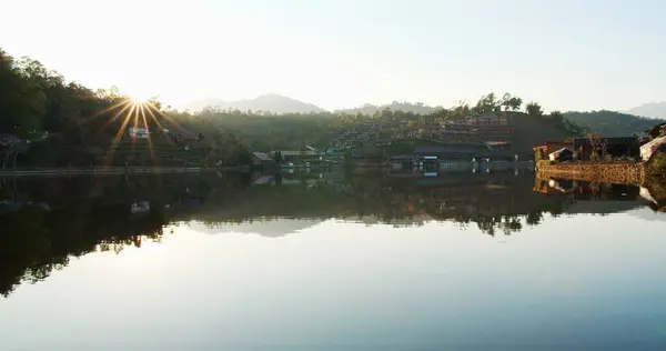 scenic landscape view of nature lake with reflection on surface and sunset sunlight in evening against village mountain hill on background at Ban Rak Thai village, Mae hong son, Northern Thailand