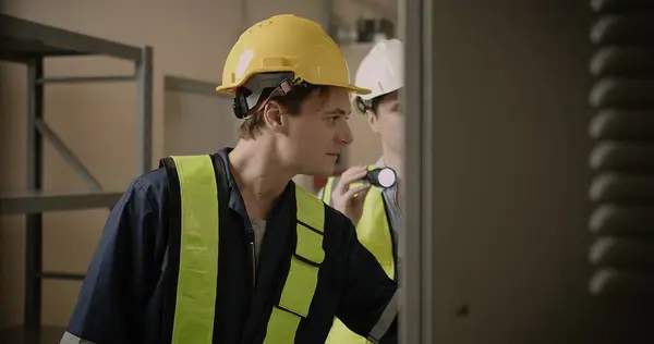 Handsome Industrial technicians Engineer in Yellow Hard Hat and Safety Vest Using Flashlights Working maintenance the electrical equipment in factory, Inspector or Safety Supervisor in industry