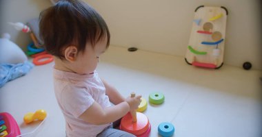 Çocuk yürümeye başlayan kız renkli bir yığın blokla oynuyor. Bloklar bir piramit şeklinde dizilmiş zeminde oturuyor ve onlara uzanıyor. Merak ve keşif kavramı