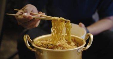 Bir insan çubukla erişte yiyor. Erişteler altın kasenin içinde.