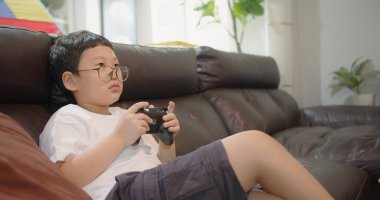 Asyalı çocuk oturma odasında kanepede oturuyor ve evde vakit geçirirken TV 'de oyun oynuyor.