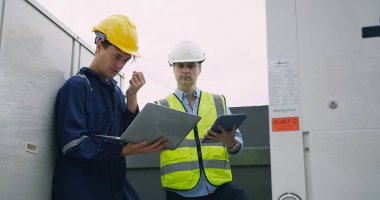 İnşaat mühendisi, inşaat müdürü ve miğferli işçi müfettişi inşaat alanının çatısındaki proje çalışmaları hakkında dizüstü bilgisayarlı toplantı yapıyorlar.