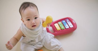 Yerde üzerinde anahtar olan bir oyuncakla bir bebek oturuyor. Bebek kameraya tuhaf bir ifadeyle bakıyor.