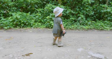 Safari kıyafeti giymiş şirin bir çocuk ve yemyeşil yeşilliklerle çevrili Doğa Yolu 'nu keşfeden bir şapka..