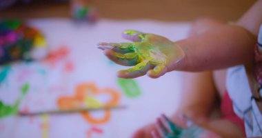 Yaratıcı Sanat Aktivitesi için beyaz bir kağıda el izi boyayan, yaratıcılığı ve sanatsal ifadeyi gösteren, yaratıcılığı ve duyusal oyunu keşfeden bir çocuk elinin yakın çekimi.