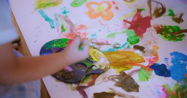 Bir çocuk el renkli resimlerle kağıt üzerinde canlı ve soyut bir sanat yaratıyor, yaratıcılık ve hayal gücü sergiliyor ve Oyuncu Sanatsal Vuruşlarda Yaratıcı Fırça darbeleri sergiliyor