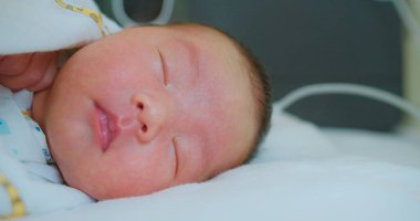 Yeni doğmuş bir bebeğin, hastane odasında yumuşak bir battaniyeye sarılı, huzur içinde uyuduğu yakın plan..