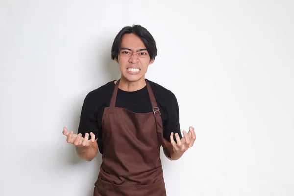 一个穿着棕色围裙的恼怒的亚洲咖啡师的画像 用手指做着愤怒的手势 白色背景上的孤立图像 — 图库照片