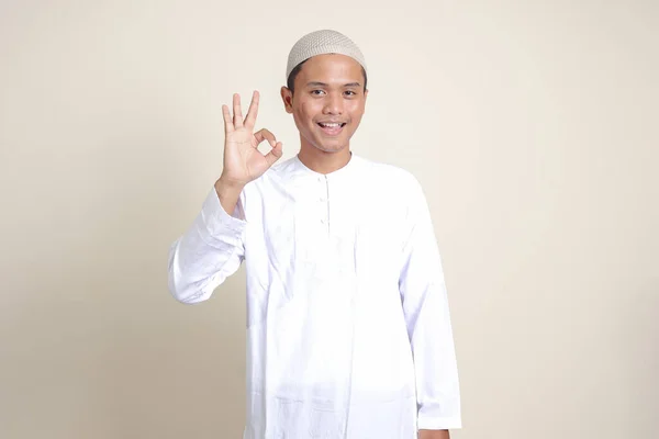 亚洲有魅力的穆斯林男子的画像 他身穿白衬衫 头戴便帽 手感不错 面带微笑地看着相机 广告概念 灰色背景上的孤立图像 — 图库照片