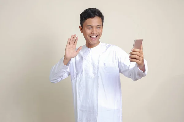 亚洲有魅力的穆斯林男子穿着白衬衫 为自己或自己拍照 在视频通话中打招呼和挥手的肖像 灰色背景上的孤立图像 — 图库照片