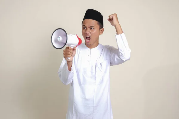 メガホンを使用して大声で話すSkullcapと白いシャツの魅力的なアジアのイスラム教徒の男性の肖像画は 製品を促進します 広告コンセプト 灰色の背景に孤立した画像 — ストック写真