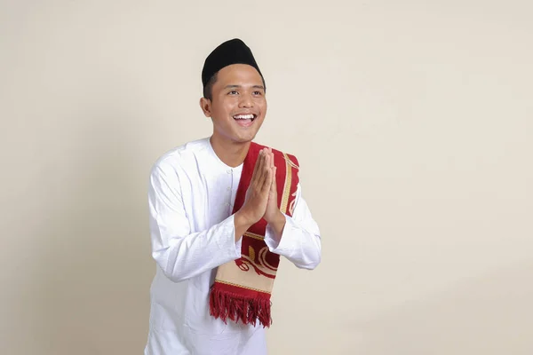 亚洲有魅力的穆斯林男子的画像 身穿白衬衫 头戴小帽 表示道歉和欢迎手势 灰色背景上的孤立图像 — 图库照片