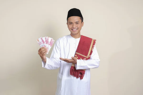 一位身穿白衬衫的有魅力的亚洲穆斯林男子的画像 一边指着侧面 一边展示着十万卢比 金融和储蓄概念 灰色背景上的孤立图像 — 图库照片