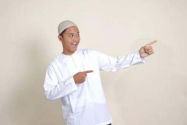 商品を示すSkullcapと彼の手と指で側面に指して白いシャツの魅力的なアジアのイスラム教徒の男性の肖像画 広告コンセプト 灰色の背景に孤立した画像 — ストック写真