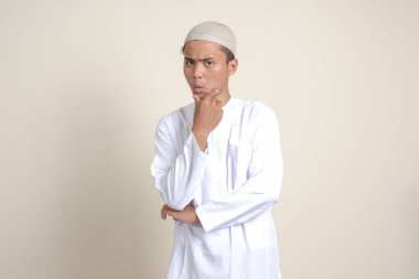 Beyaz gömlekli çekici Asyalı Müslüman adamın portresi, eli çenesinde soru sormayı düşünüyor. Gri arkaplanda izole edilmiş resim