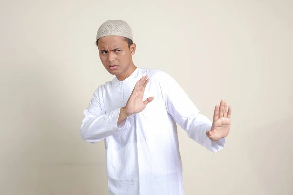 何か悪いことを避けるために手のジェスチャーを形成Skullcapと白いシャツの魅力的なアジアのイスラム教徒の男の肖像画 灰色の背景に孤立した画像 — ストック写真