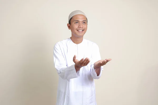 亚洲有魅力的穆斯林男子的画像 穿着白衬衫 展示产品 手指头指向侧面 灰色背景上的孤立图像 — 图库照片