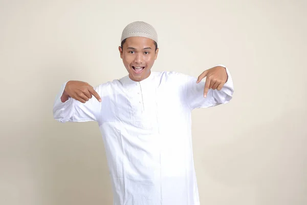 商品を示すSkullcapと彼の手と指で側面に指して白いシャツの魅力的なアジアのイスラム教徒の男性の肖像画 広告コンセプト 灰色の背景に孤立した画像 — ストック写真