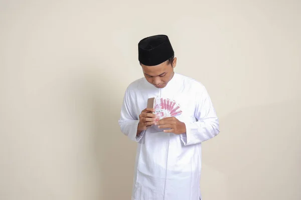 一个穿着白衬衫的有魅力的亚洲穆斯林男子的画像 在使用手机时显示出10万卢比 金融和储蓄概念 灰色背景上的孤立图像 — 图库照片