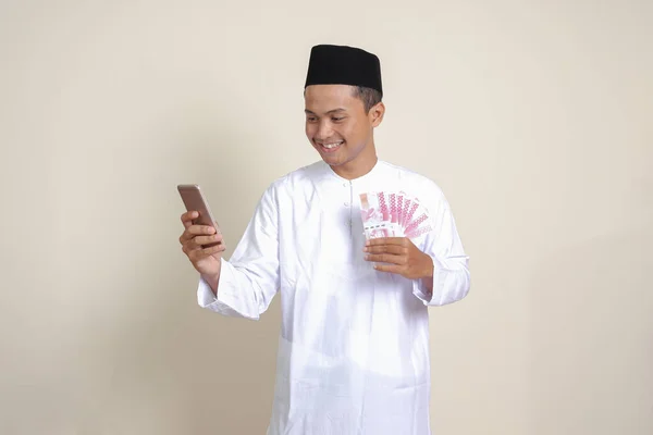 셔츠를 매력적 아시아 남성의 모습은 전화를 사용하면서 루피아를 배경의 고립된 — 스톡 사진