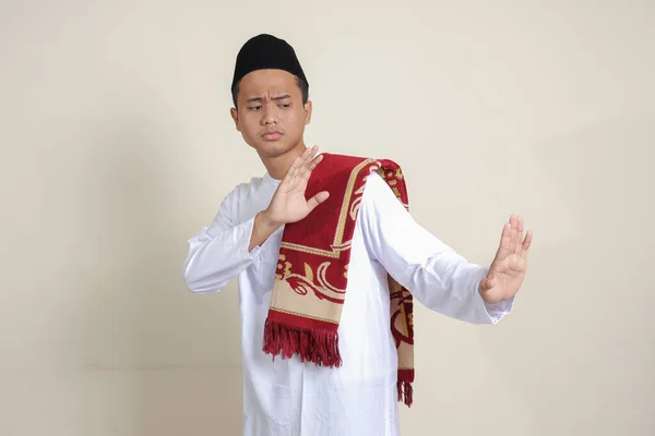 亚洲有魅力的穆斯林男子的画像 他身穿白衬衫 头戴便帽 摆出一种手势 以逃避某件事或坏事 灰色背景上的孤立图像 — 图库照片