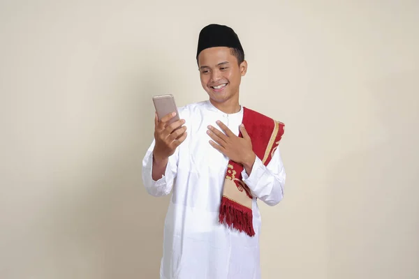 白いシャツを着た魅力的なアジア系イスラム教徒の男性の肖像画は 自分自身や自撮りを撮影し ハイと言って ビデオ通話中に手を振っています 灰色の背景に孤立した画像 — ストック写真