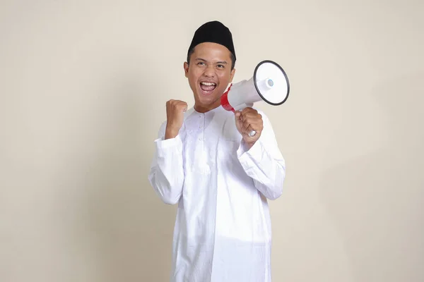 メガホンを使用して大声で話すSkullcapと白いシャツの魅力的なアジアのイスラム教徒の男性の肖像画は 製品を促進します 広告コンセプト 灰色の背景に孤立した画像 — ストック写真