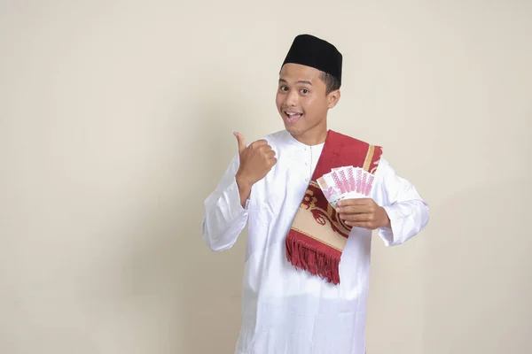 一位身穿白衬衫的有魅力的亚洲穆斯林男子的画像 一边指着侧面 一边展示着十万卢比 金融和储蓄概念 灰色背景上的孤立图像 — 图库照片