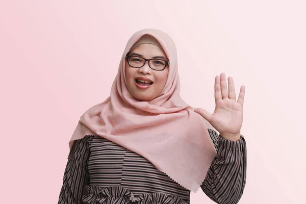 Portrait of cheerful Asian woman with hijab, smiling and showing five fingers gesture, waving hand. Advertising concept. Isolated image on pink background