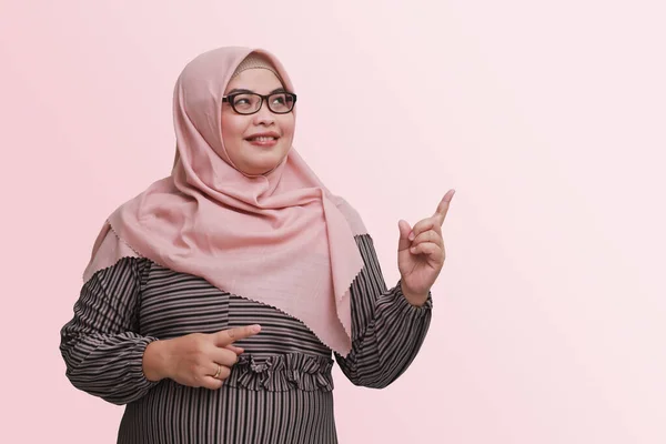 ヒジャーブと陽気なアジアの女性の肖像 製品を示し 何かを指して笑顔 広告コンセプト ピンクの背景に隔離された画像 — ストック写真