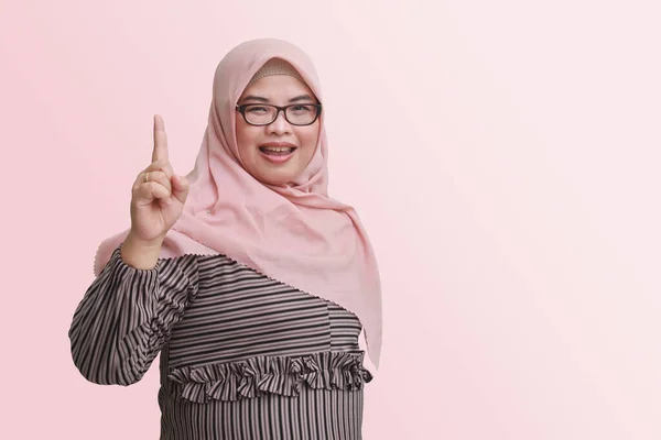 带着头巾的快乐的亚洲女人的画像 指着她的食指 提醒她该做些什么 广告概念 粉色背景上的孤立图像 — 图库照片