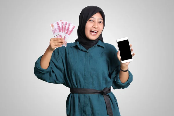 带头巾的兴奋的亚洲穆斯林妇女的肖像 展示了10万卢比 同时展示了空白屏幕的手机模型 金融和储蓄概念 白色背景上的孤立图像 — 图库照片