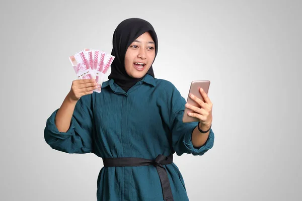 흥분한 아시아인 히잡의 핸드폰을 루피아를 배경에 고립된 이미지 — 스톡 사진