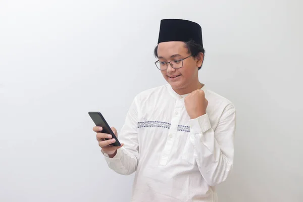 年轻的亚洲穆斯林男子举起拳头 庆祝胜利或在手机上得到好消息的肖像 白色背景上的孤立图像 — 图库照片