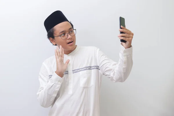 一个面带微笑的年轻的亚洲穆斯林男子为自己拍照或打视频电话 打招呼和挥挥手的画像 白色背景上的孤立图像 — 图库照片