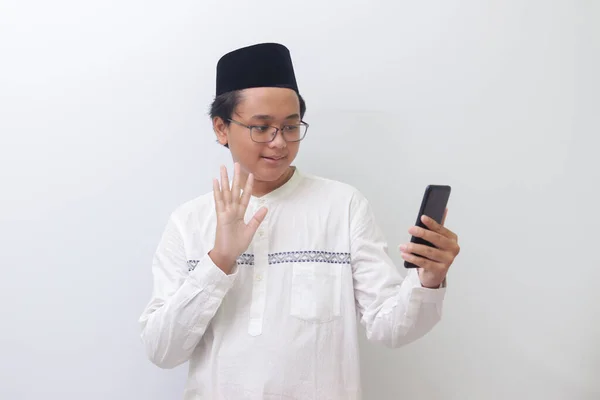 一个面带微笑的年轻的亚洲穆斯林男子为自己拍照或打视频电话 打招呼和挥挥手的画像 白色背景上的孤立图像 — 图库照片