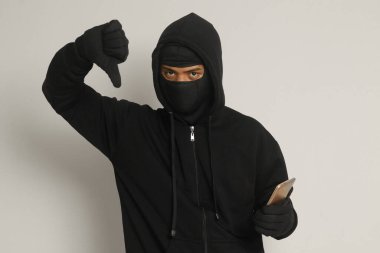 Siyah kapüşonlu ve maskeli gizemli bir adamın portresi cep telefonunda hackleme faaliyetleri yapıyor, elinde akıllı telefon tutan bir bilgisayar korsanı. Gri arkaplanda izole edilmiş resim