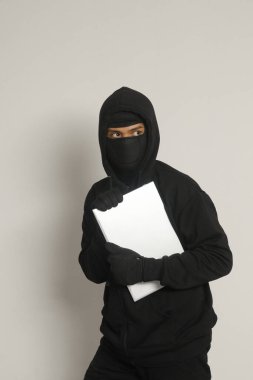 Siyah kapüşonlu ve maskeli gizemli hırsız dizüstü bilgisayar çalıp sıvışıyor. Gri arkaplanda izole edilmiş resim