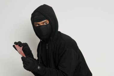 Siyah kapüşonlu ve maskeli gizemli bir adamın portresi. Kurbandan 100.000 rupia çalmış. Gri arkaplanda izole edilmiş resim
