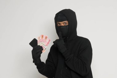 Siyah kapüşonlu ve maskeli gizemli bir adamın portresi. Kurbandan 100.000 rupia çalmış. Gri arkaplanda izole edilmiş resim