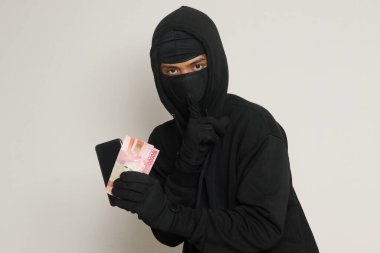 Siyah kapüşonlu ve maskeli gizemli bir adamın portresi. Kurbandan 100.000 rupia çalmış. Gri arkaplanda izole edilmiş resim