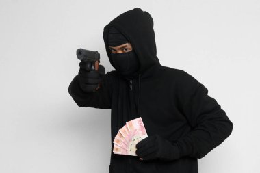 Siyah kapüşonlu ve maskeli gizemli bir adamın portresi. Elinde 100 bin rupiah banknot tutarken silahla ateş ediyor. Para sızdırıyor. Gri arkaplanda izole edilmiş resim
