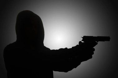 Siyah kapüşonlu, tabanca tutan, silahla ateş eden gizemli bir adam. Siluet ve karanlık konsept görüntüsü