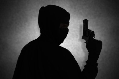 Siyah kapüşonlu, tabanca tutan, silahla ateş eden gizemli bir adam. Siluet ve karanlık konsept görüntüsü