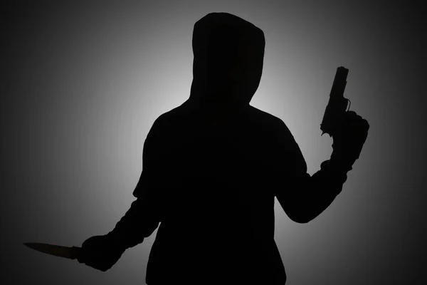 ピストルを持った黒いパーカーを着た謎の男がナイフを持ちながら銃で撃つ シルエットと暗いコンセプト画像 — ストック写真