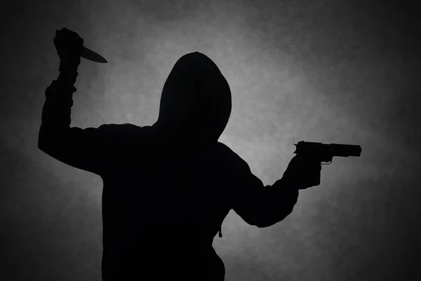 Mysterious man wearing black hoodie holding a pistol, shooting with a gun while holding a knife. Silhouette and dark concept image