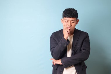 Asyalı genç bir iş adamının portresi rahat giyinmiş gözlerini kapatmış, çok düşünüyor. Mavi arkaplanda izole edilmiş resim