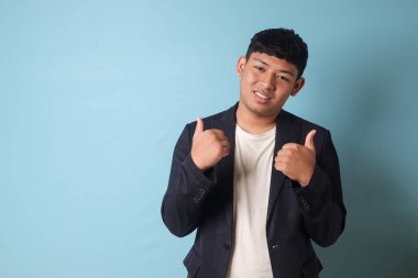 Asyalı genç bir iş adamının portresi. Yüzünde mutlu bir ifade var. Mavi arkaplanda izole edilmiş resim