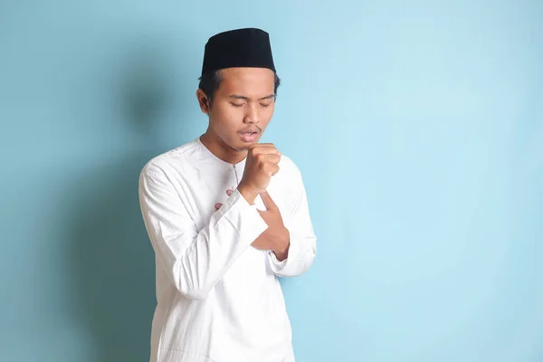 亚洲有魅力的穆斯林男子穿着白衬衫 手心捂着嘴 另一只手牵着胸部咳嗽的画像 蓝色背景上的孤立图像 — 图库照片